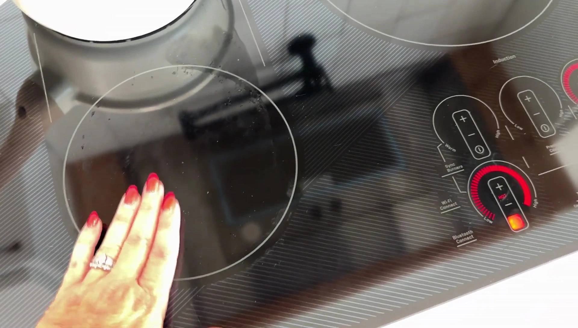 Hand touching the cooktop surface to demonstrate its cool temperature.